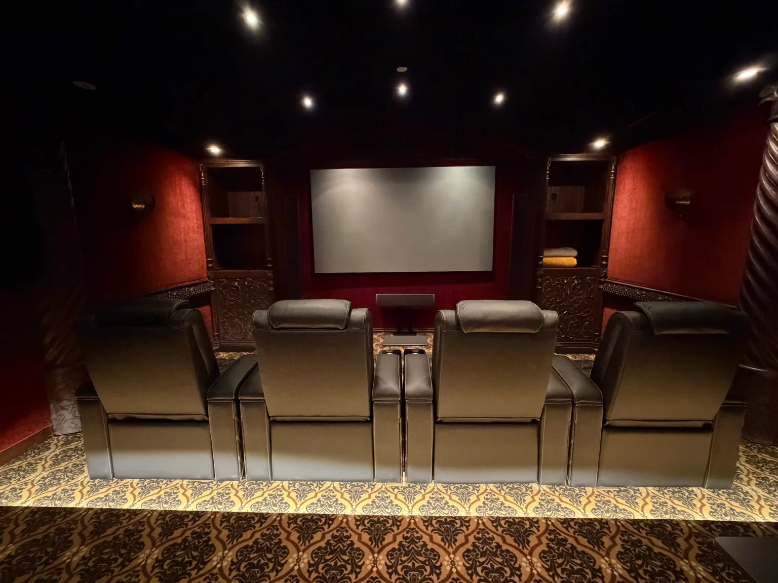 Four theater recliners facing a blank projection screen in a red dedicated home cinema