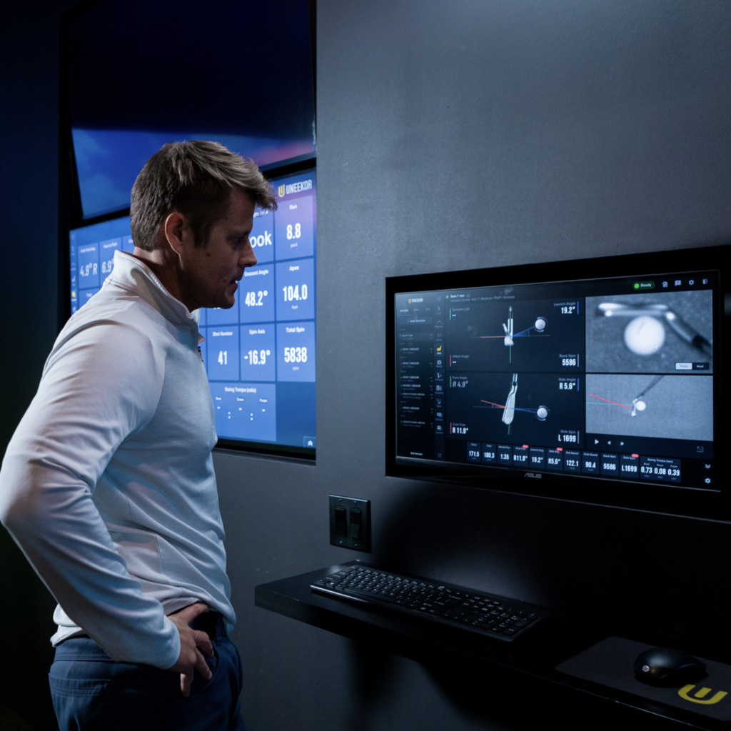 Golfer reviewing launch monitor ball and club data on simulator displays