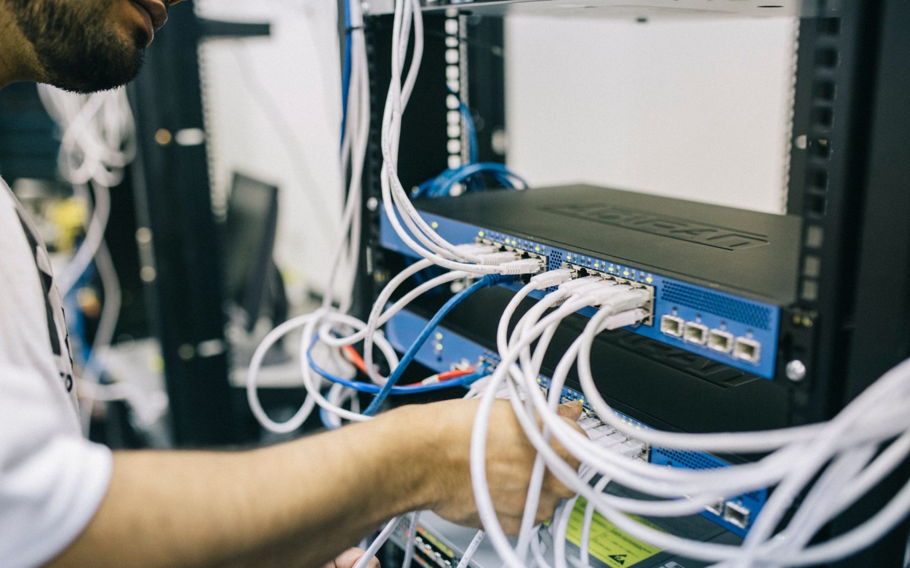 Low-voltage technician connecting structured cabling to managed network switches in an equipment rack